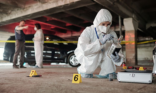 Criminological expert in coveralls inspecting empty bottle on crime scene.