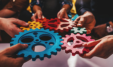 A number of people holding cogs representing team work.