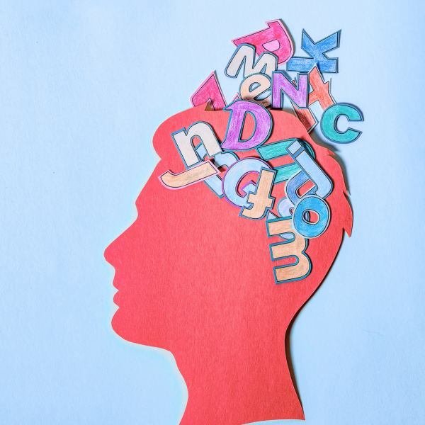 A pink silhouette of a head profile is filled with colorful, jumbled letters.